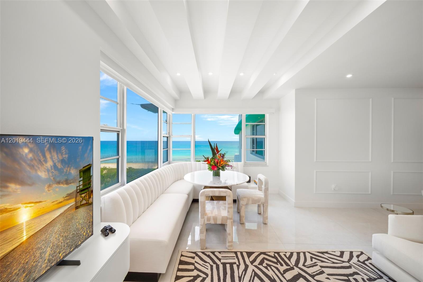 A bright dining area features a curved white banquette, round table, and ocean views — 5255 Collins Ave # 8F, Miami Beach FL 33140, MIAMI BEACH, FL