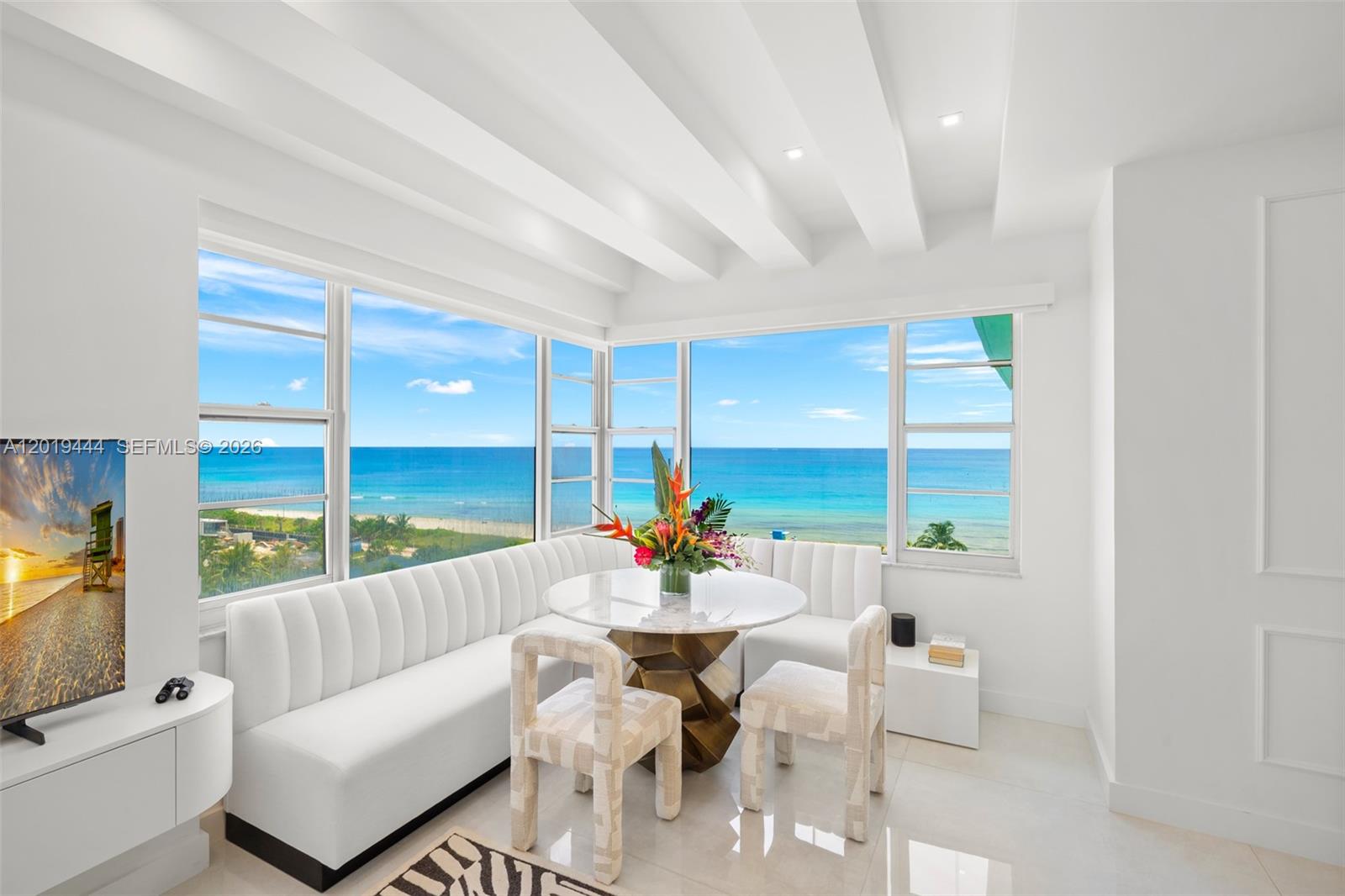 A white dining nook features a curved banquette, a marble table, and ocean views — 5255 Collins Ave # 8F, Miami Beach FL 33140, MIAMI BEACH, FL