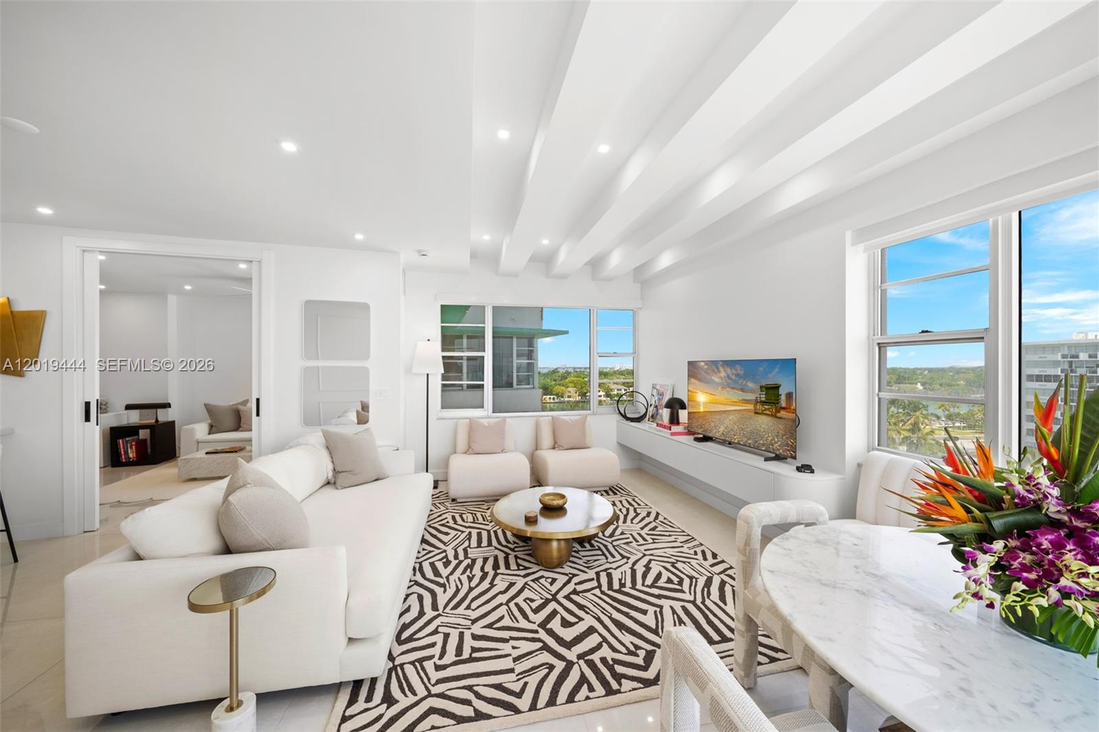 A bright living room features white furniture, a patterned rug, and a view of water — 5255 Collins Ave # 8F, Miami Beach FL 33140, MIAMI BEACH, FL