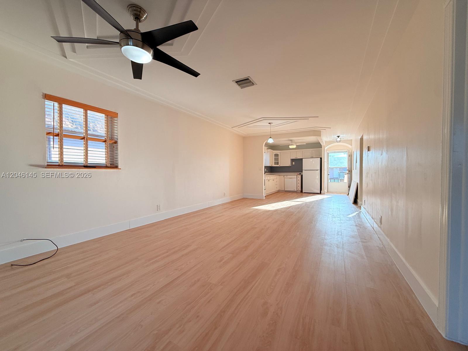 A living room with light wood flooring leads into an open kitchen with white cabinets — 2832 Fillmore St # 20, Hollywood FL 33020, HOLLYWOOD, FL