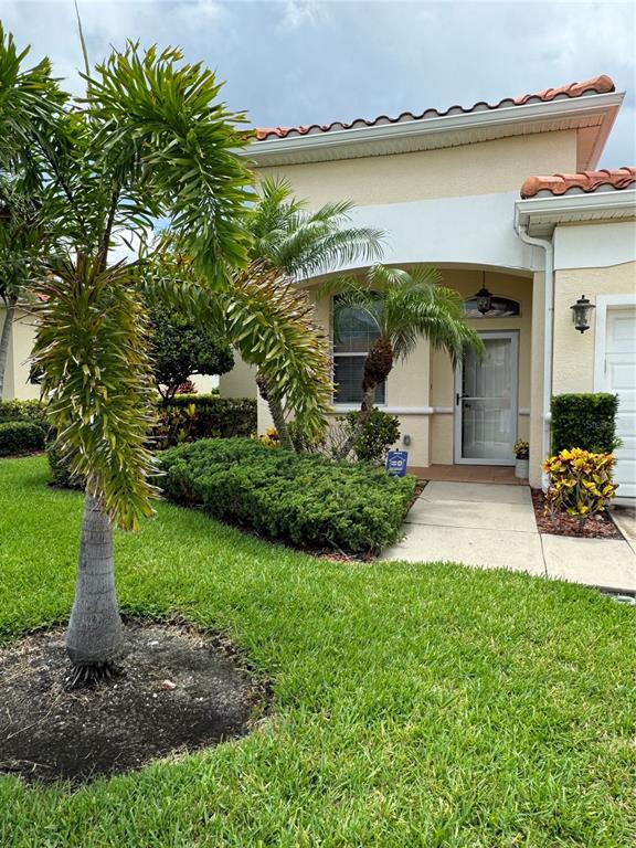 The exterior of a beige house features a palm tree, landscaping, and a front entrance — 8636 VILLANOVA DRIVE UNIT 1201, CAPE CANAVERAL, FL