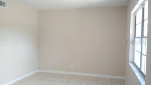 An empty room with beige walls, light-colored tile flooring, and a window with white trim — 302 S SPRING GARDEN AVENUE UNIT A06, DELAND, FL
