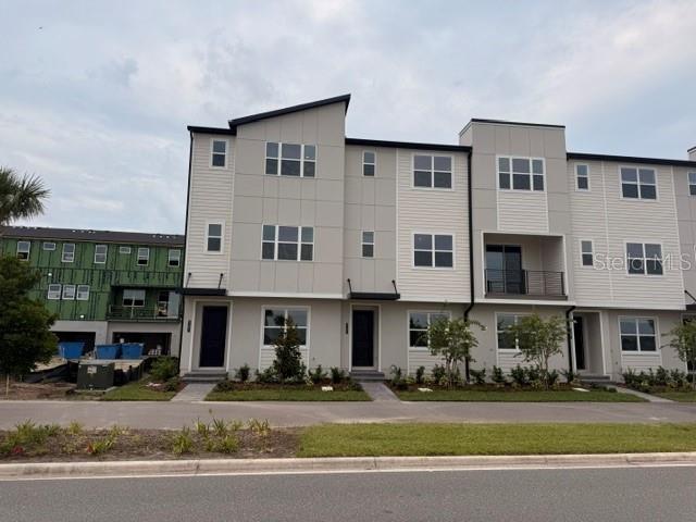 A multi-story townhouse exterior with light-colored siding and a dark roof under a cloudy sky — 9301 LUMINARY BOULEVARD, ORLANDO, FL