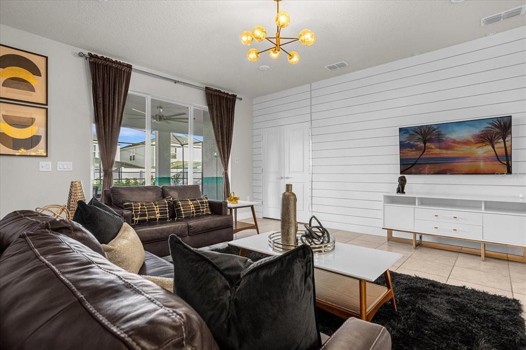 A living room features a white shiplap accent wall, dark leather furniture, and a modern chandelier — 1191 ALOHA BOULEVARD, DAVENPORT, FL