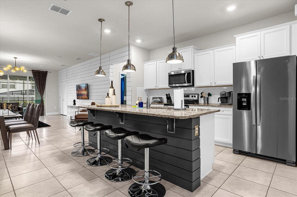 A kitchen features a dark gray island with bar seating, white cabinets, and tile flooring — 1191 ALOHA BOULEVARD, DAVENPORT, FL