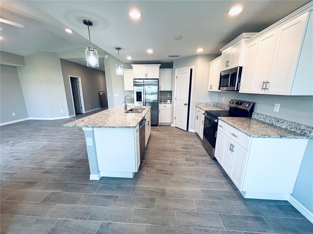 A modern kitchen features white cabinets, granite countertops, stainless steel appliances, and gray tile flooring — 415 BAYTREE DRIVE, ROTONDA WEST, FL
