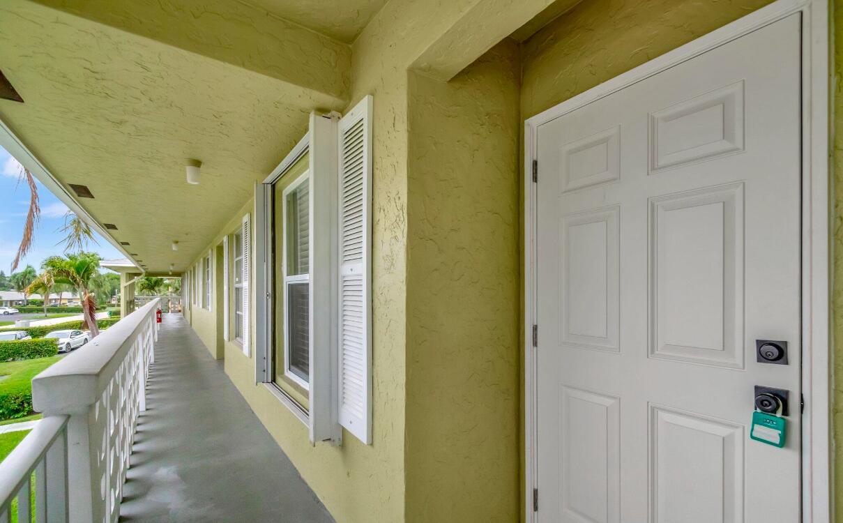 A white door with a lockbox opens onto a long, covered outdoor walkway with railings — 1140 Mahogany Way # 204, Delray Beach FL 33445, DELRAY BEACH, FL