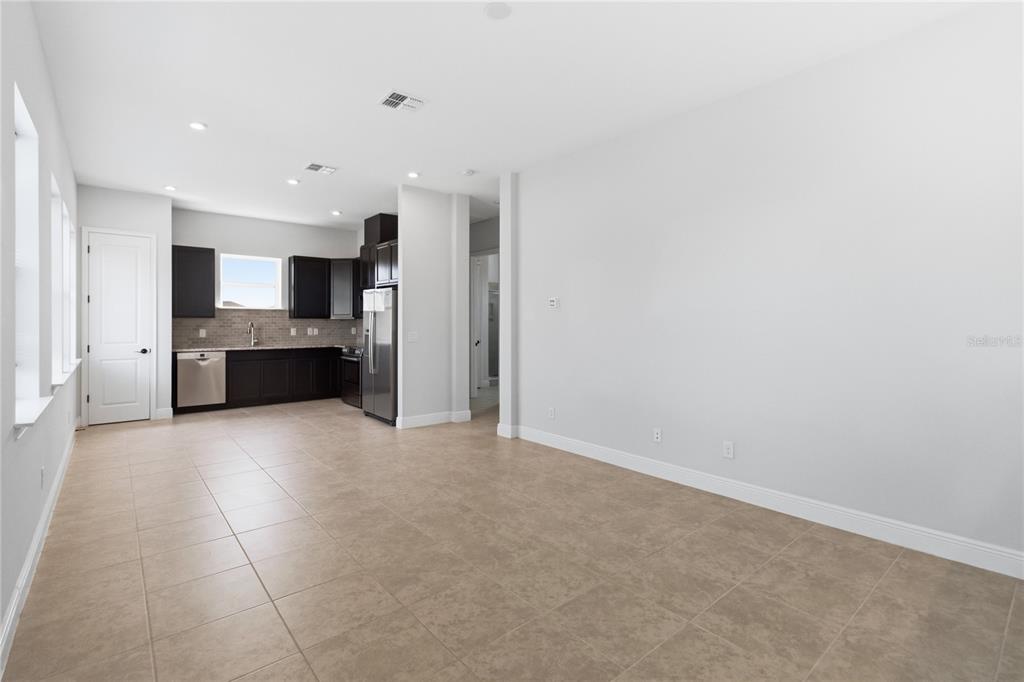An open-concept kitchen and living area features dark cabinetry, stainless steel appliances, and tile flooring — 13030 STODDART AVENUE, ORLANDO, FL