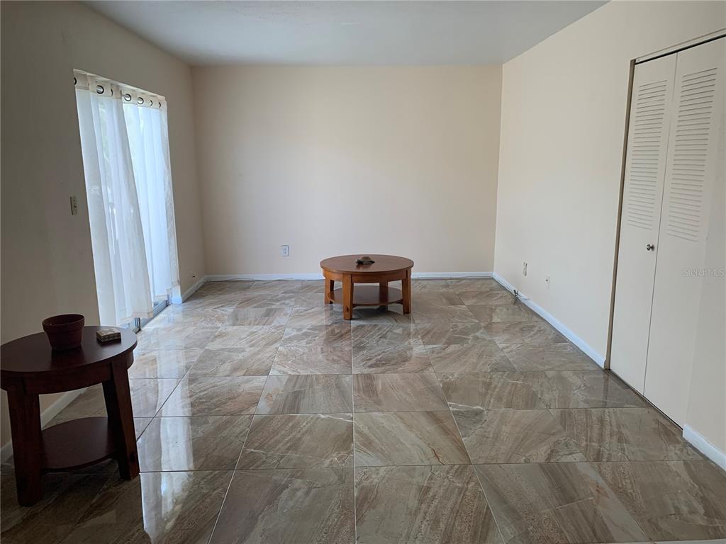 A living room features large, polished brown tile flooring, a round coffee table, and sliding doors — 1799 N HIGHLAND AVENUE UNIT 170, CLEARWATER, FL