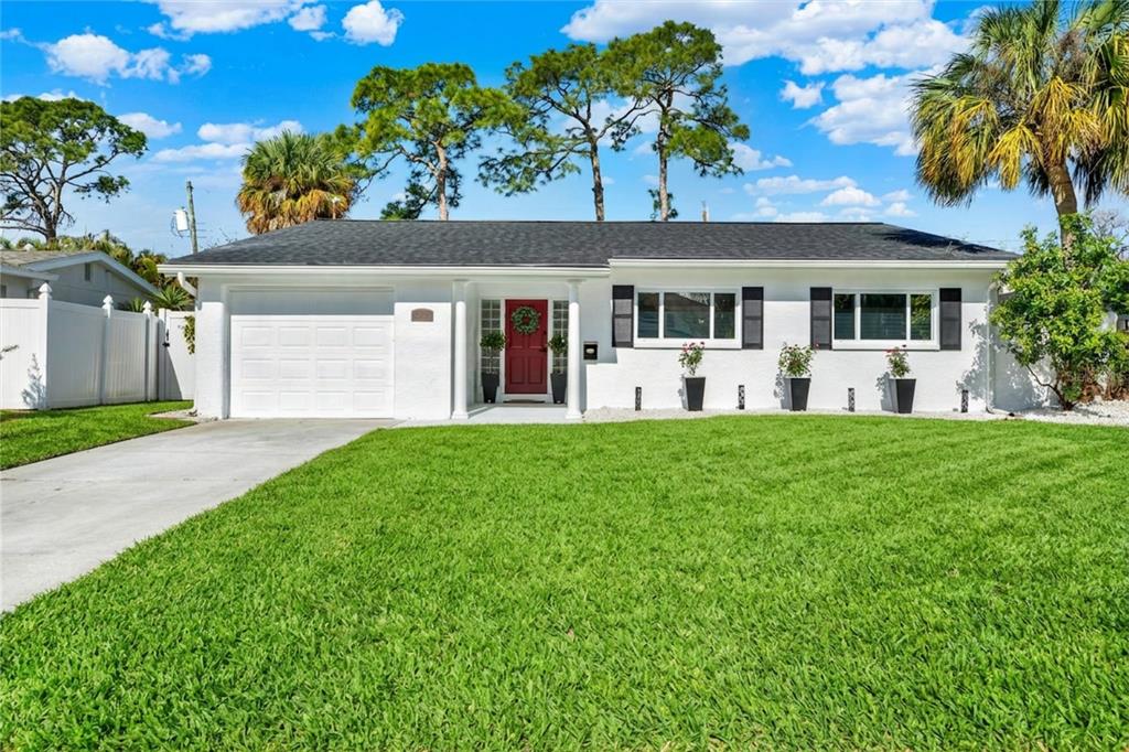 A single-story white house with a red front door, black shutters, and a green lawn — 4510 NE HELENA STREET NE, ST PETERSBURG, FL