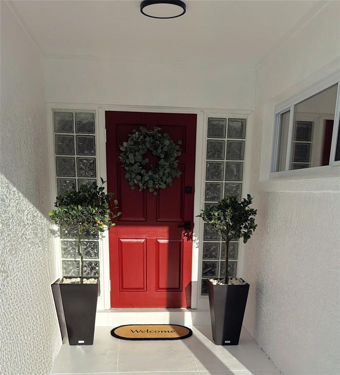 A red front door is flanked by glass block sidelights and two potted topiary trees — 4510 NE HELENA STREET NE, ST PETERSBURG, FL