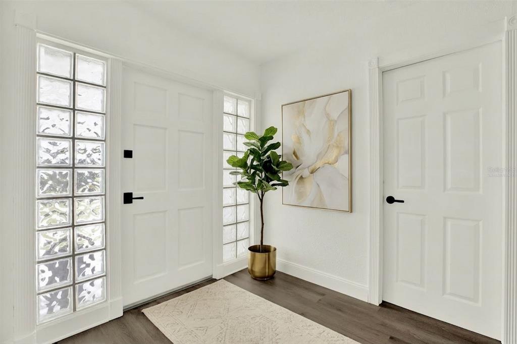 A bright entryway features a white door with glass block sidelights, a potted plant, and artwork — 4510 NE HELENA STREET NE, ST PETERSBURG, FL