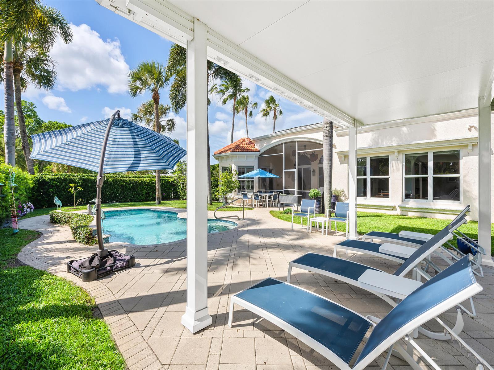 A patio with lounge chairs and a swimming pool sits beside a house with palm trees — 2370 Deer Creek Trail, Deerfield Beach FL 33442, DEERFIELD BEACH, FL
