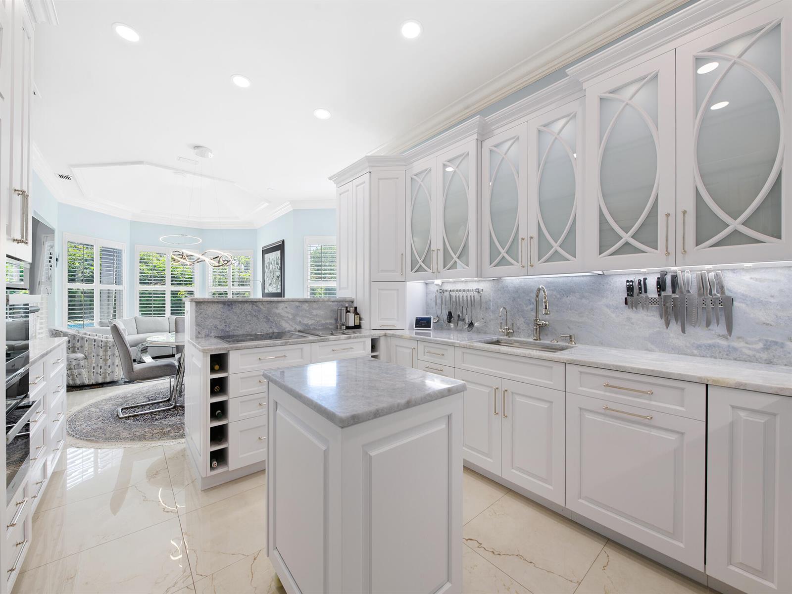 A bright kitchen features white cabinetry, marble countertops, a small island, and a dining area — 2370 Deer Creek Trail, Deerfield Beach FL 33442, DEERFIELD BEACH, FL