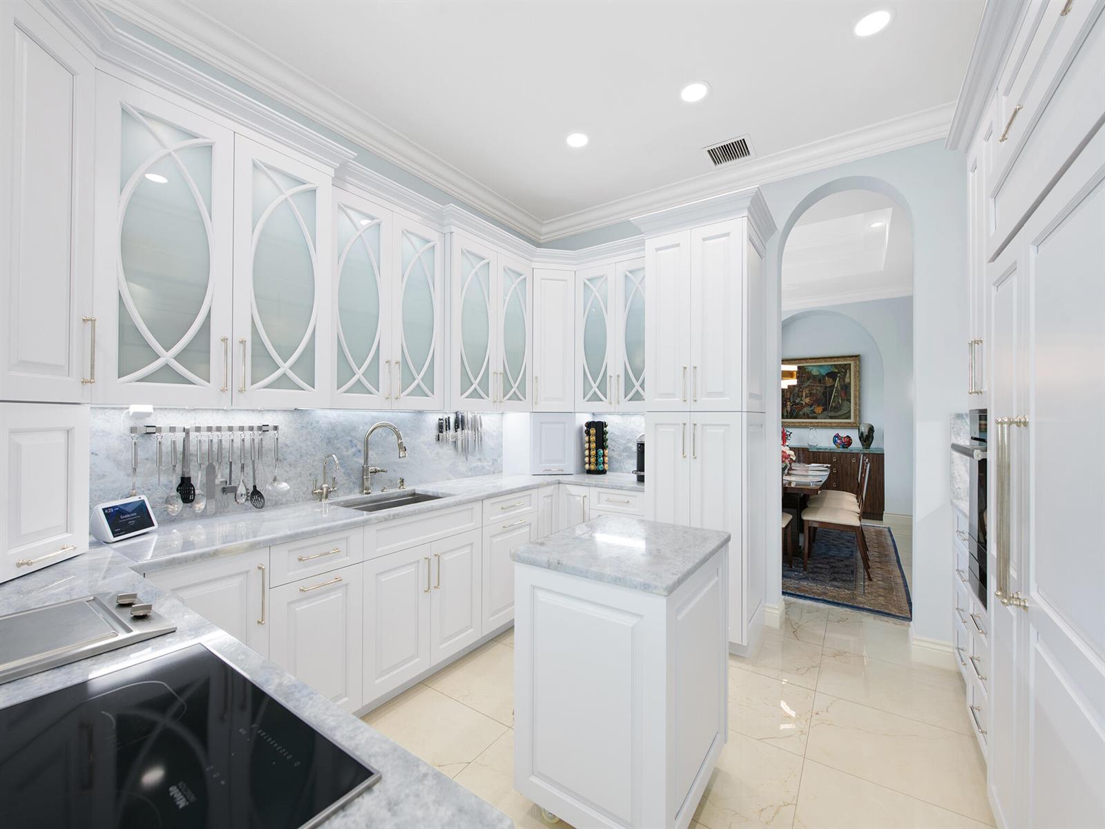 A white kitchen features marble countertops, glass-paneled upper cabinets, and a small rolling island — 2370 Deer Creek Trail, Deerfield Beach FL 33442, DEERFIELD BEACH, FL