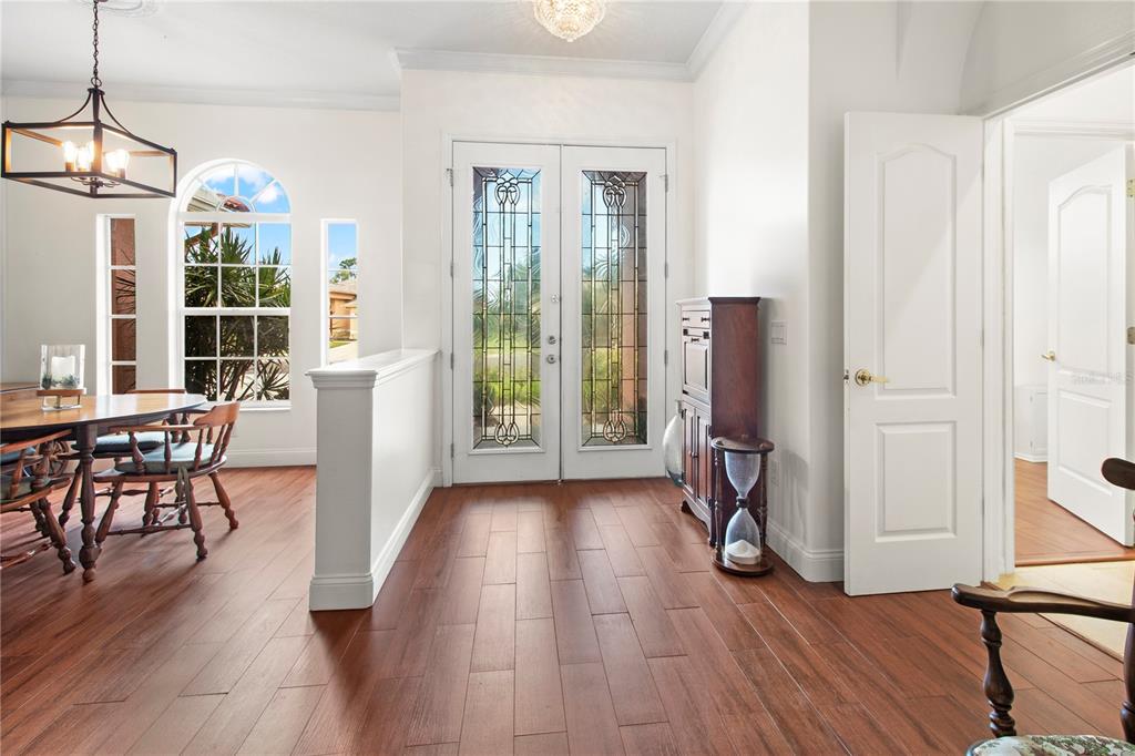 A foyer with wood-look flooring leads to double glass-paneled doors and an adjacent dining area — 7341 FEATHERSTONE BOULEVARD, SARASOTA, FL