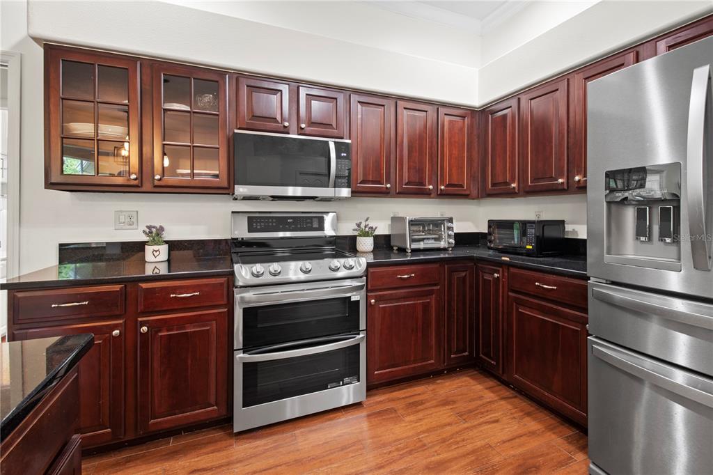 A kitchen features dark wood cabinets, black countertops, stainless steel appliances, and wood-look flooring — 7341 FEATHERSTONE BOULEVARD, SARASOTA, FL