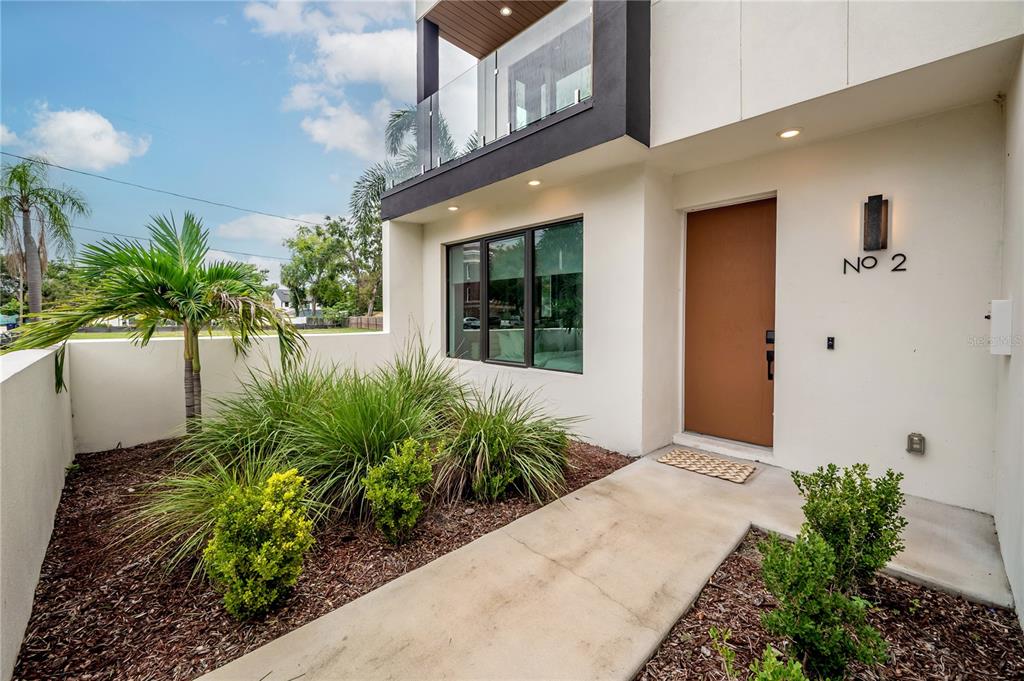 The exterior of a modern home features a brown front door, glass balcony, and landscaping — 117 W GLADYS STREET UNIT 2, TAMPA, FL