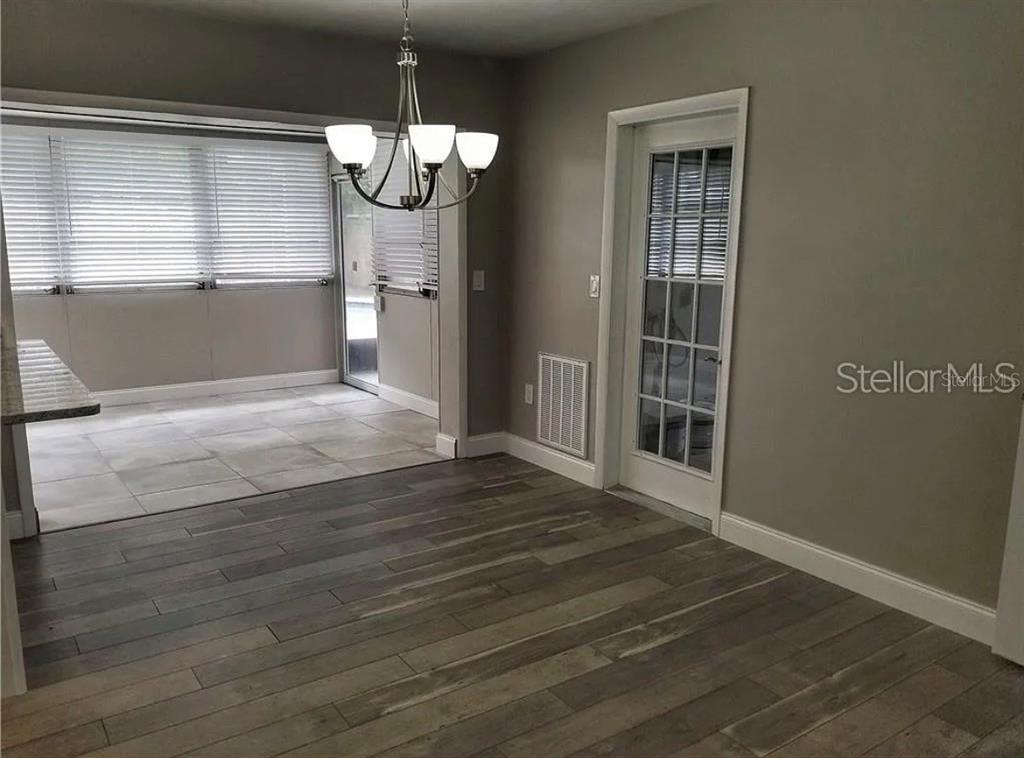 A dining area with wood-look flooring leads into a tiled sunroom through an open doorway — 1664 S EVERGREEN AVENUE, CLEARWATER, FL