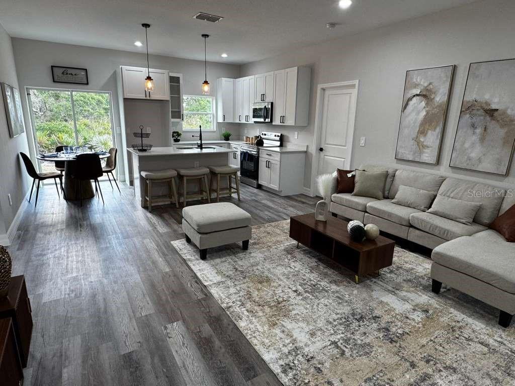 An open-concept kitchen and living area features white cabinetry, a center island, and wood-look flooring — 300 CASPIAN TERN AVENUE, SEBRING, FL