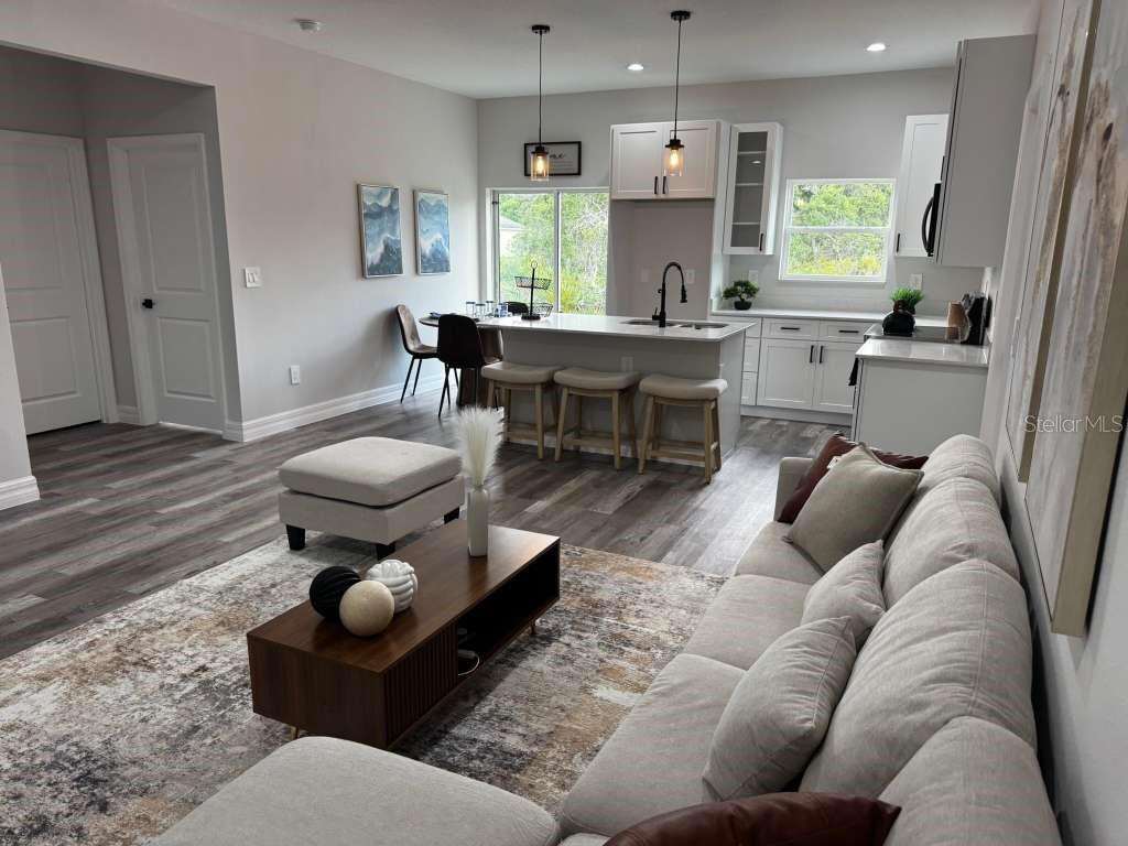 An open-concept living room and kitchen featuring light wood flooring, white cabinetry, and neutral furniture — 300 CASPIAN TERN AVENUE, SEBRING, FL