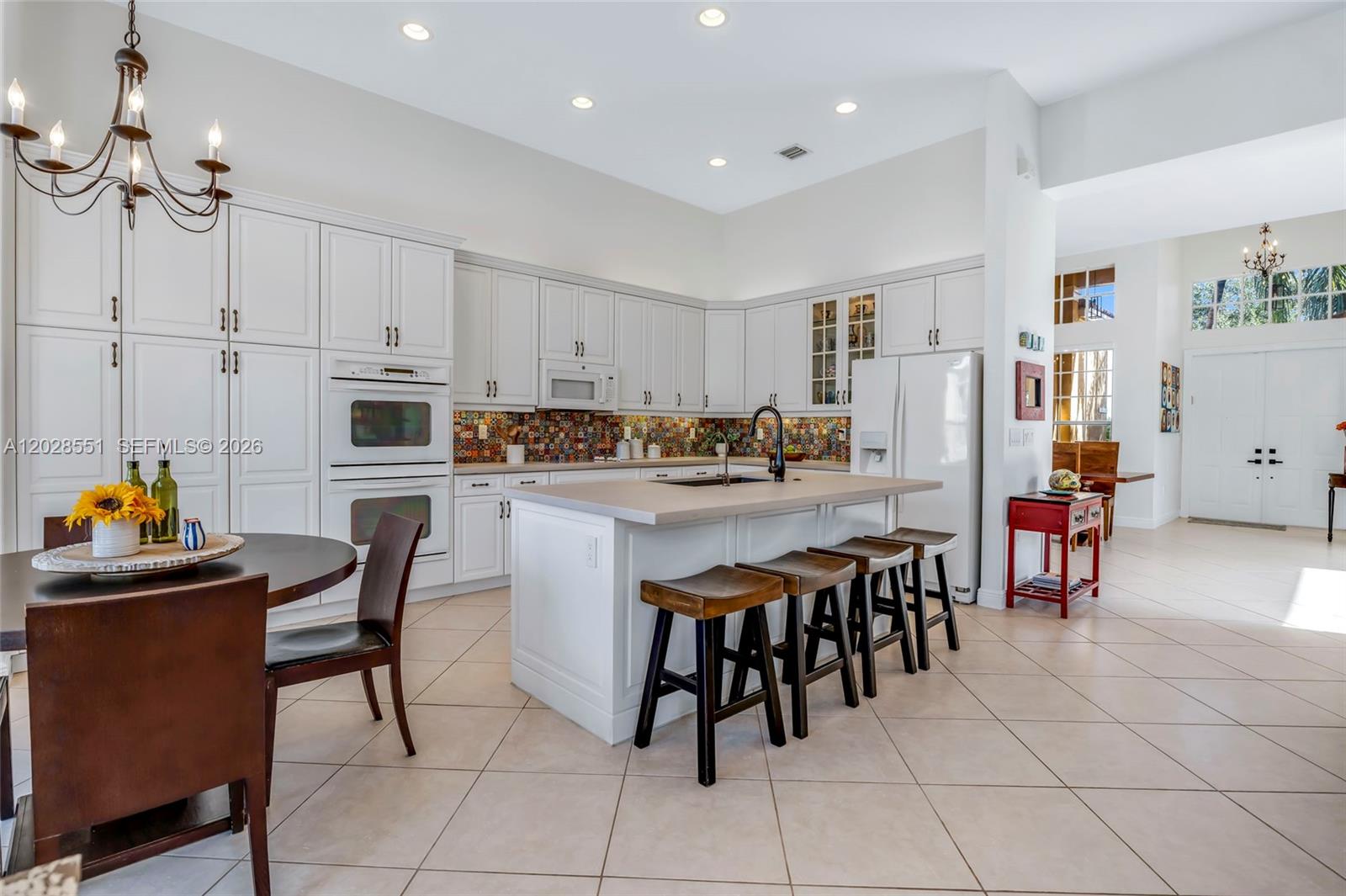 A white kitchen features a central island with bar stools and a colorful tile backsplash — 19442 SW 39th St, Miramar FL 33029, MIRAMAR, FL