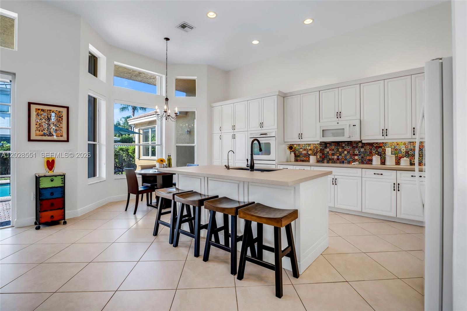 A kitchen features white cabinetry, a central island with bar stools, and a colorful backsplash — 19442 SW 39th St, Miramar FL 33029, MIRAMAR, FL