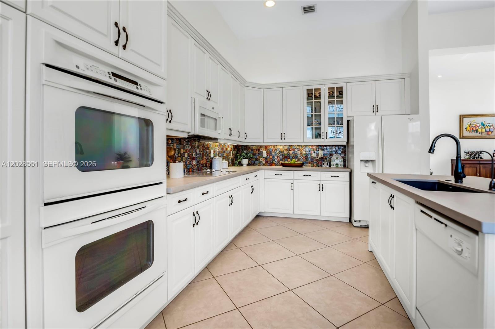 A white kitchen features a colorful mosaic backsplash, double wall ovens, and tile flooring — 19442 SW 39th St, Miramar FL 33029, MIRAMAR, FL