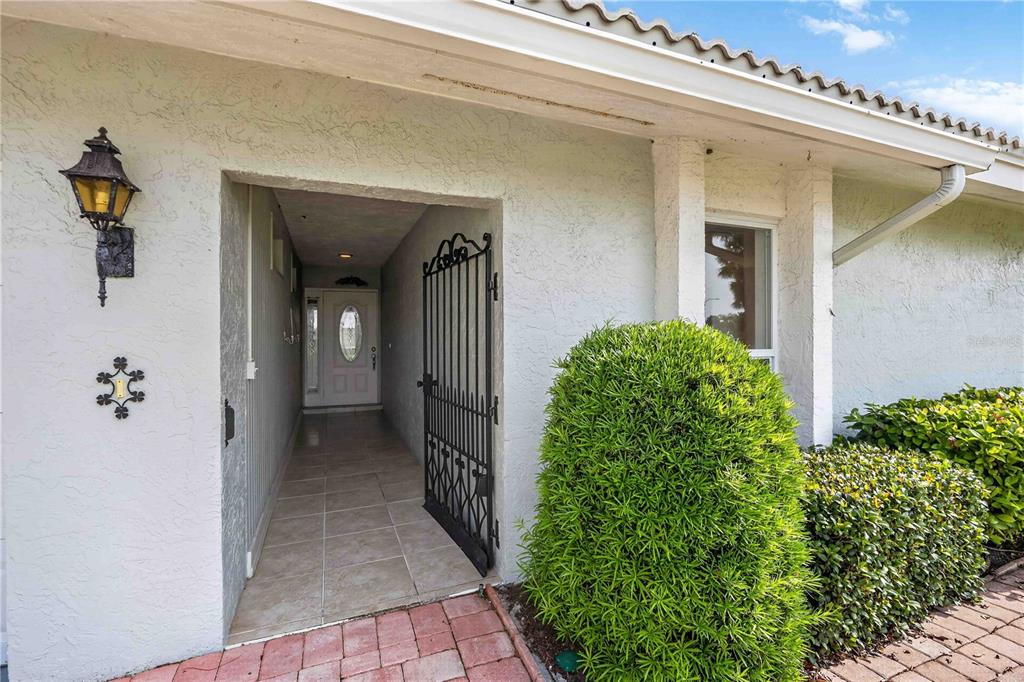 A gated walkway leads to the front entrance of a house with stucco walls — 6510 11TH AVENUE W, BRADENTON, FL