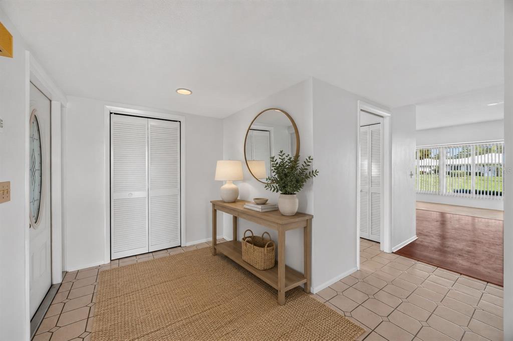 A bright entryway features a console table, round mirror, louvered closet doors, and tile flooring — 6510 11TH AVENUE W, BRADENTON, FL