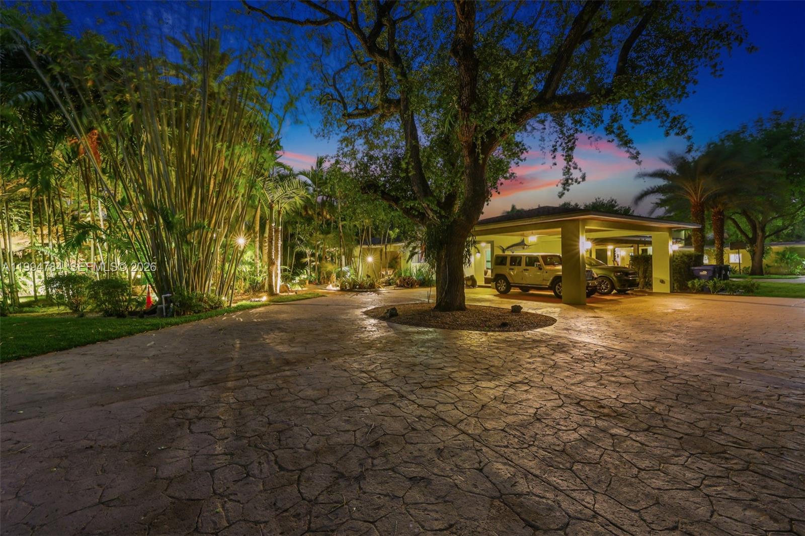 A paved driveway leads to a covered carport beside a large tree at dusk — 9234 SW 112th St, Miami FL 33176, MIAMI, FL