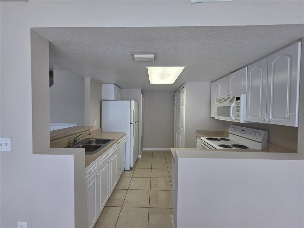 A galley-style kitchen features white cabinets, white appliances, a double sink, and beige tile flooring — 103 COCONUT PALM WAY, DAVENPORT, FL
