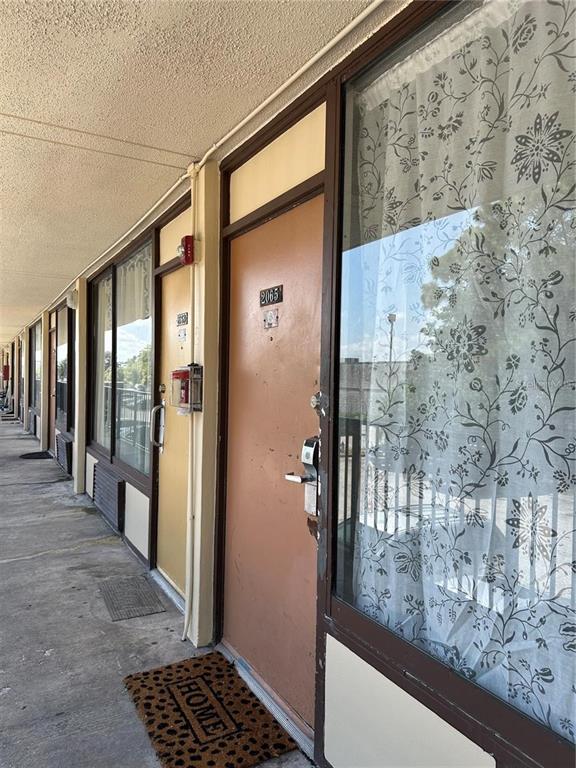 An exterior walkway leads to a row of apartment doors with large windows and floral curtains — 7900 S ORANGE BLOSSOM TRAIL UNIT 2065, ORLANDO, FL