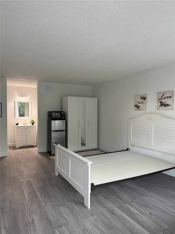 A bedroom with light wood-look flooring, a white bed frame, a wardrobe, and a mini-fridge — 7900 S ORANGE BLOSSOM TRAIL UNIT 2065, ORLANDO, FL