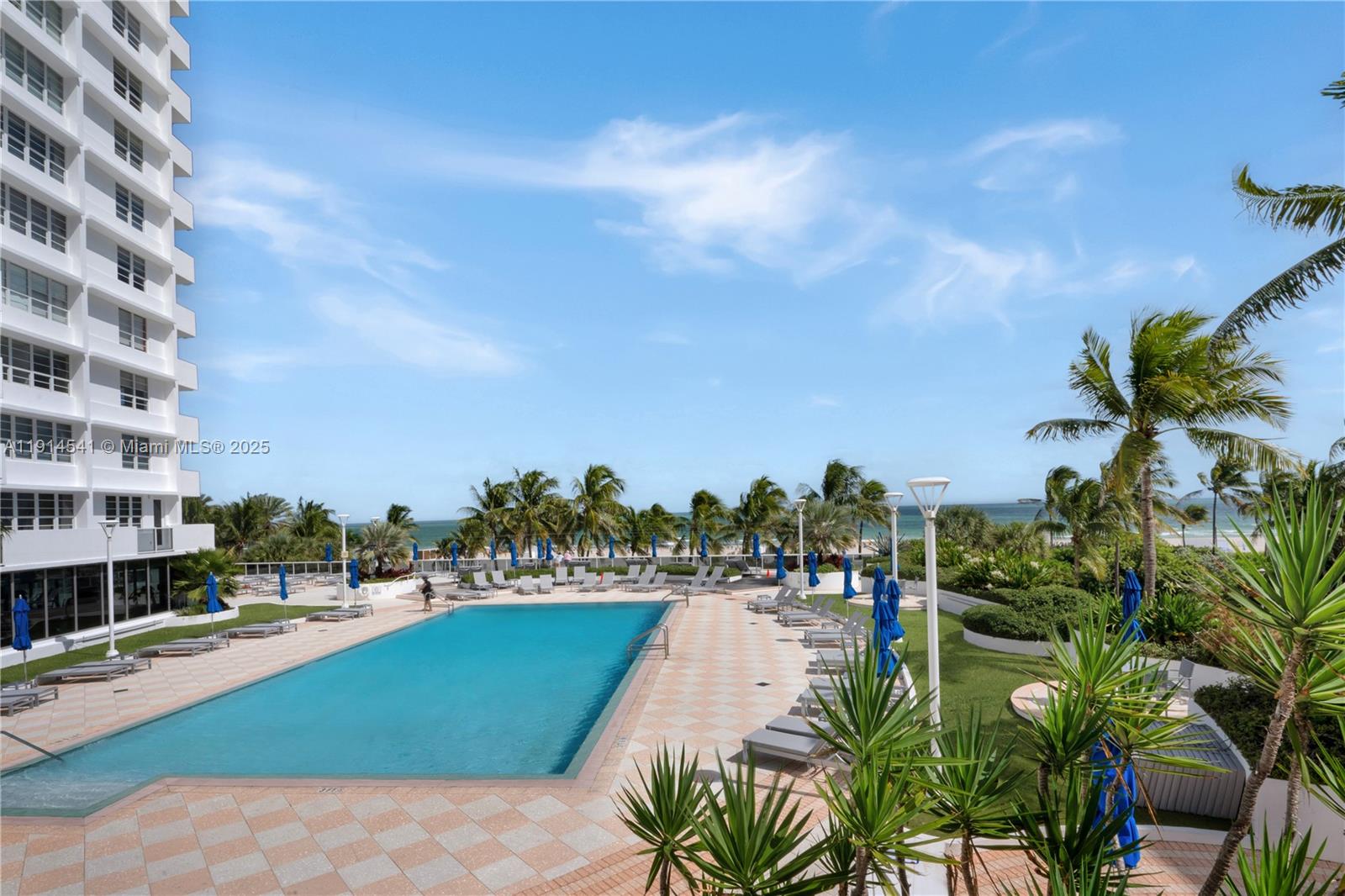 An outdoor swimming pool is surrounded by lounge chairs, palm trees, and a tall building — 100 Lincoln Rd # 607, Miami Beach FL 33139, MIAMI BEACH, FL