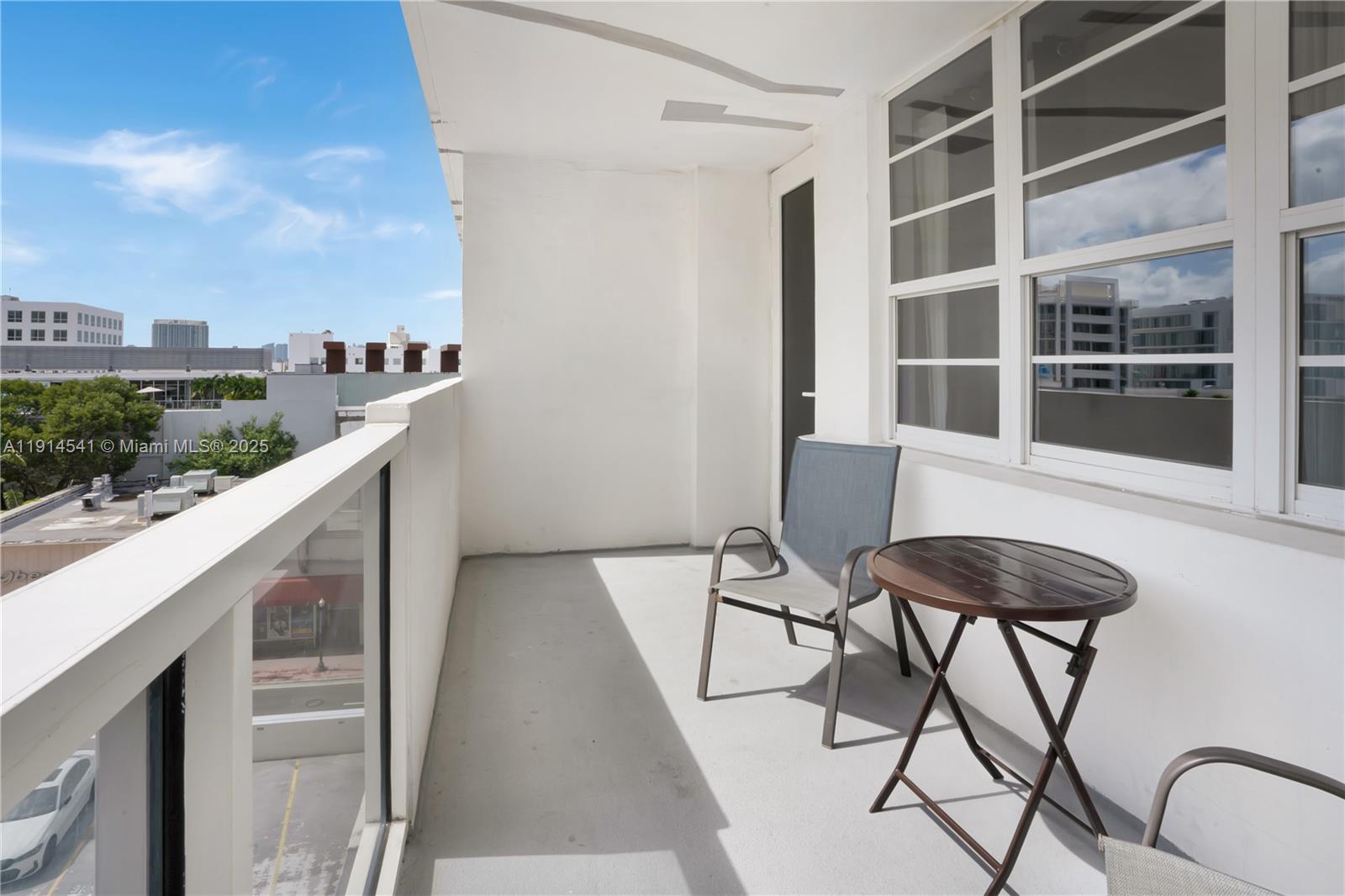 A balcony features a small table, two chairs, and a glass railing overlooking a city — 100 Lincoln Rd # 607, Miami Beach FL 33139, MIAMI BEACH, FL
