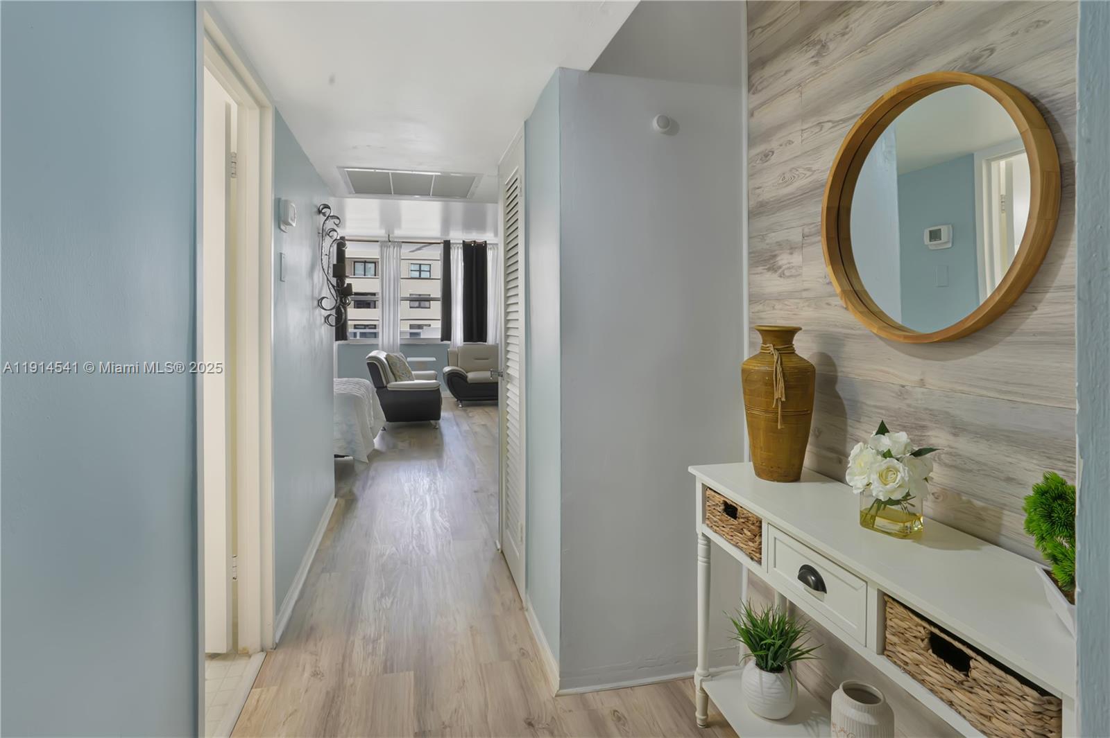 A hallway with light blue walls leads to a living area with wood-look flooring — 100 Lincoln Rd # 607, Miami Beach FL 33139, MIAMI BEACH, FL