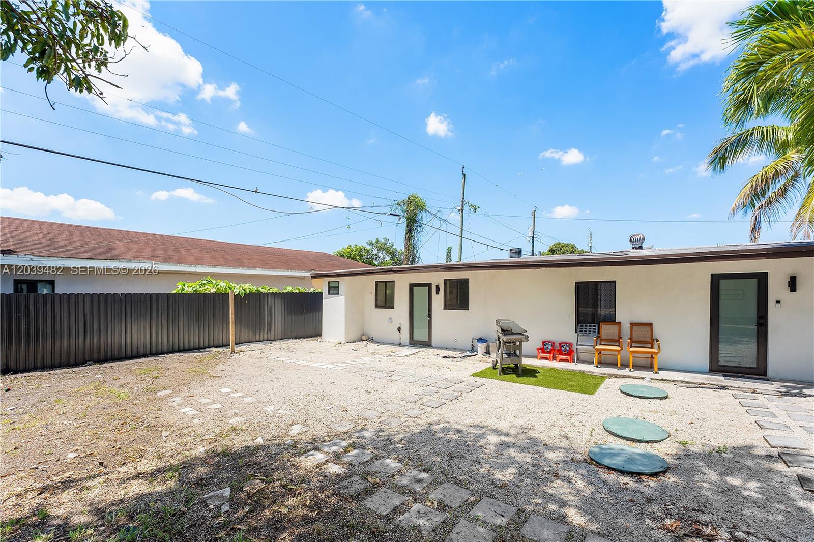 A gravel backyard features a white house exterior, a fence, and outdoor seating — 3040 NW 93rd St, Miami FL 33147, MIAMI, FL