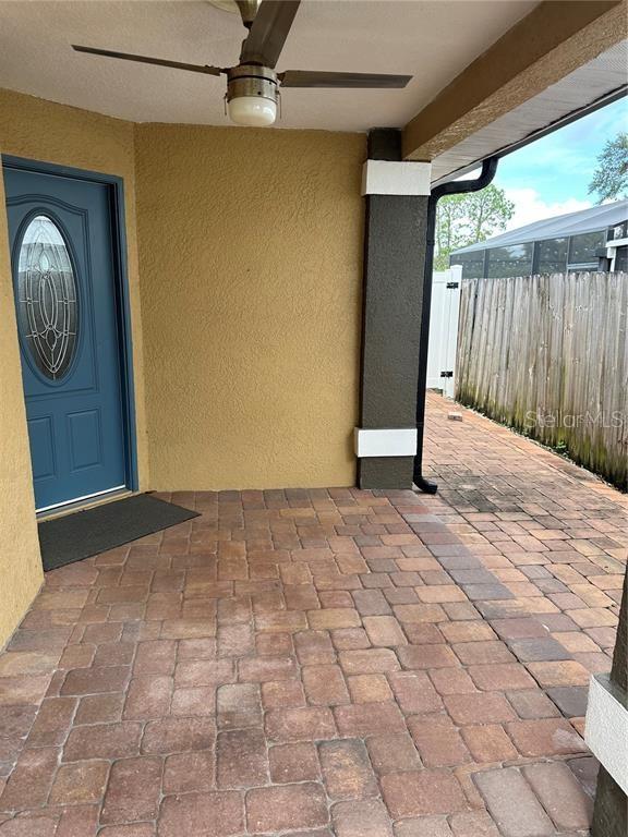A covered patio features a blue front door, a ceiling fan, and brick paver flooring — 2986 STILLWATER DRIVE, KISSIMMEE, FL