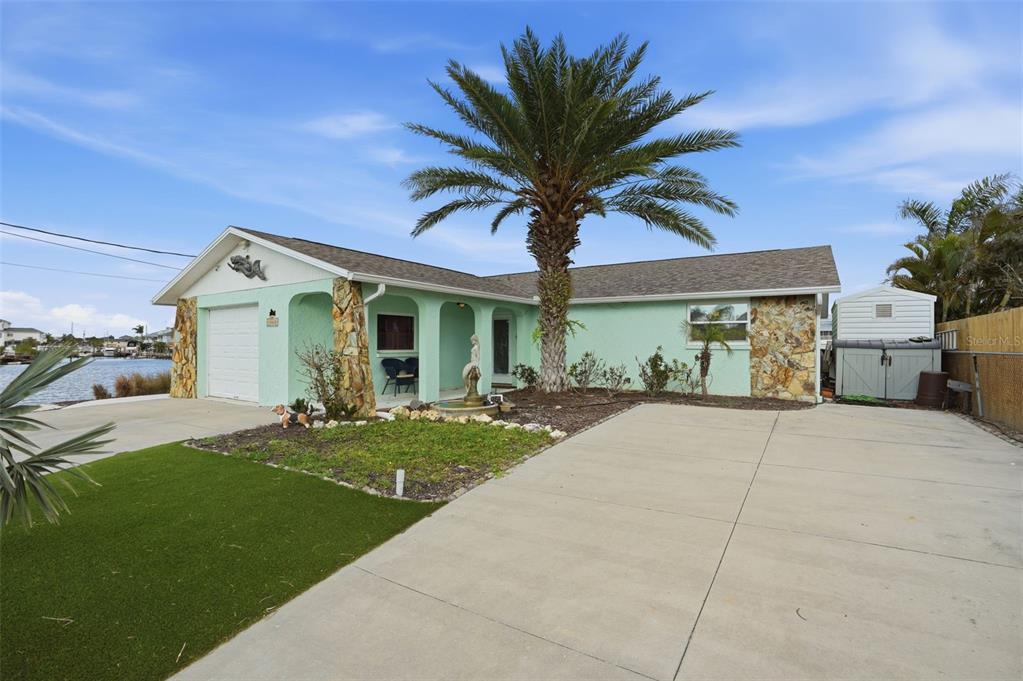 A light green house with a stone-accented exterior, a palm tree, and a concrete driveway — 13822 MALCOLM AVENUE, HUDSON, FL