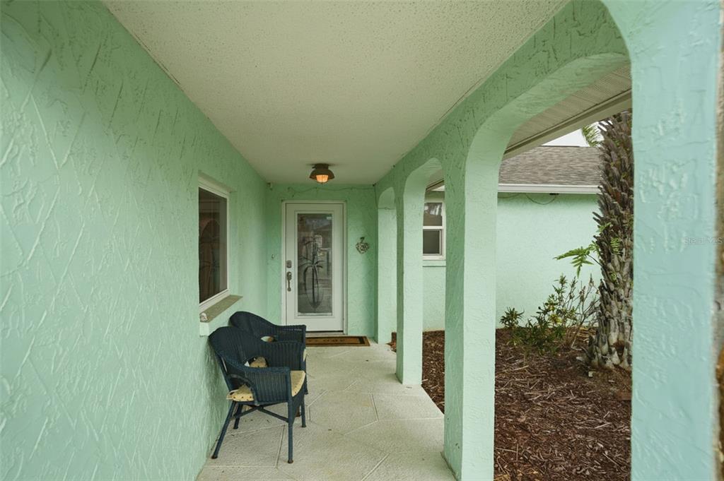 A covered porch with light green stucco walls, arched openings, and two wicker chairs — 13822 MALCOLM AVENUE, HUDSON, FL