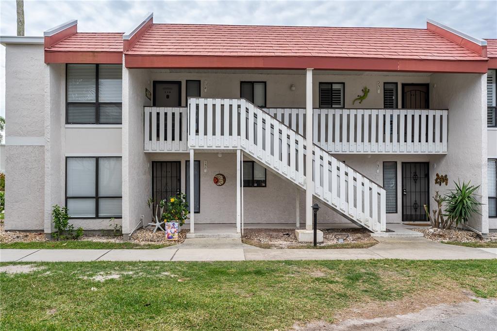A two-story apartment building features a white stucco exterior, red roof, and an outdoor staircase — 1801 GULF DRIVE N UNIT 238, BRADENTON BEACH, FL