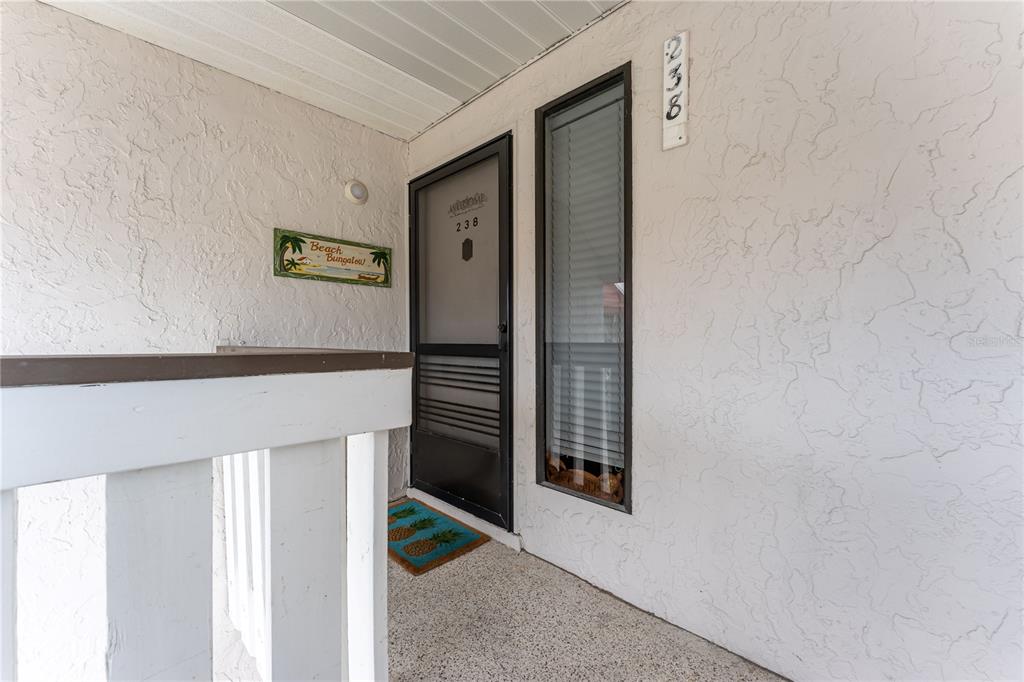 The exterior entrance of a residence features a screen door, a window, and a pineapple mat — 1801 GULF DRIVE N UNIT 238, BRADENTON BEACH, FL