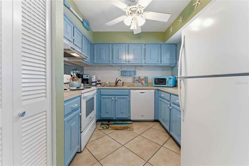 A kitchen features blue cabinets, white appliances, tile flooring, and a ceiling fan — 1801 GULF DRIVE N UNIT 238, BRADENTON BEACH, FL