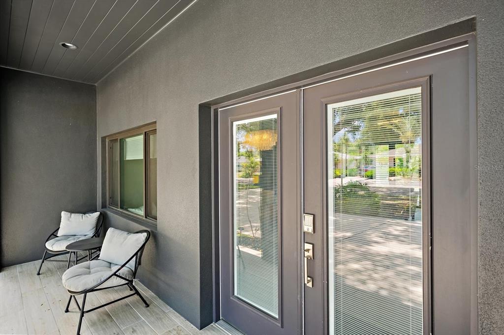 A covered patio features gray stucco walls, a tiled floor, two chairs, and double glass doors — 1905 TULIP DRIVE, SARASOTA, FL