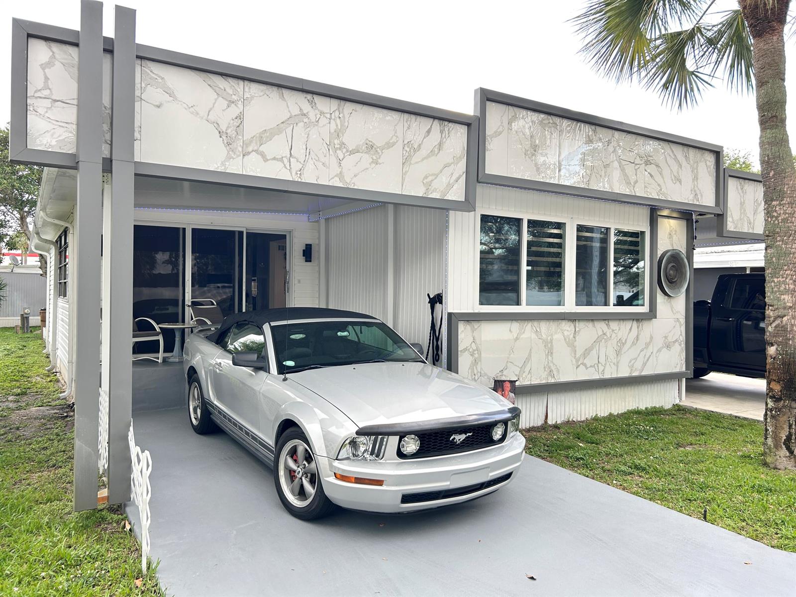 A silver convertible Mustang is parked under the carport of a house with marble-patterned siding — 111 Alamanda Lane, Deerfield Beach FL 33442, DEERFIELD BEACH, FL