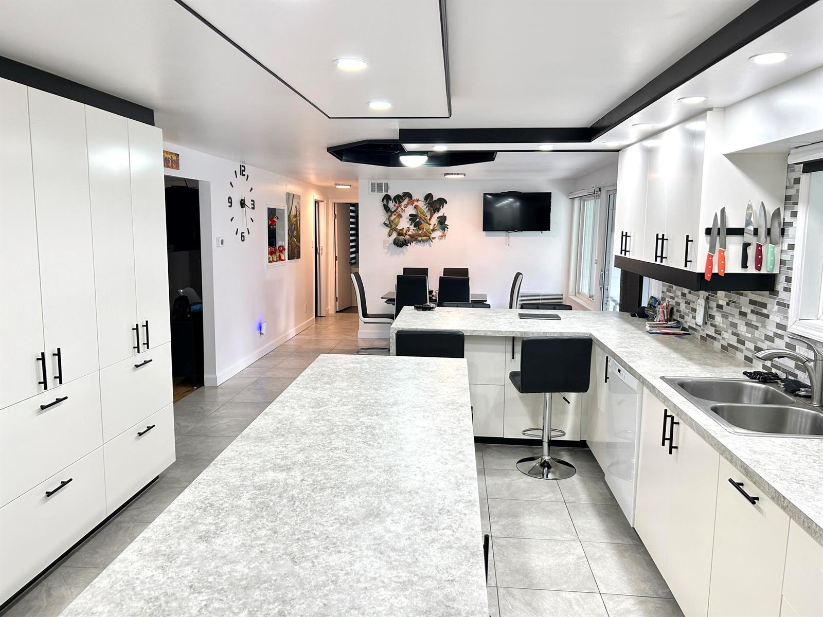A modern kitchen features white cabinets, a large island, and a dining area beyond — 111 Alamanda Lane, Deerfield Beach FL 33442, DEERFIELD BEACH, FL