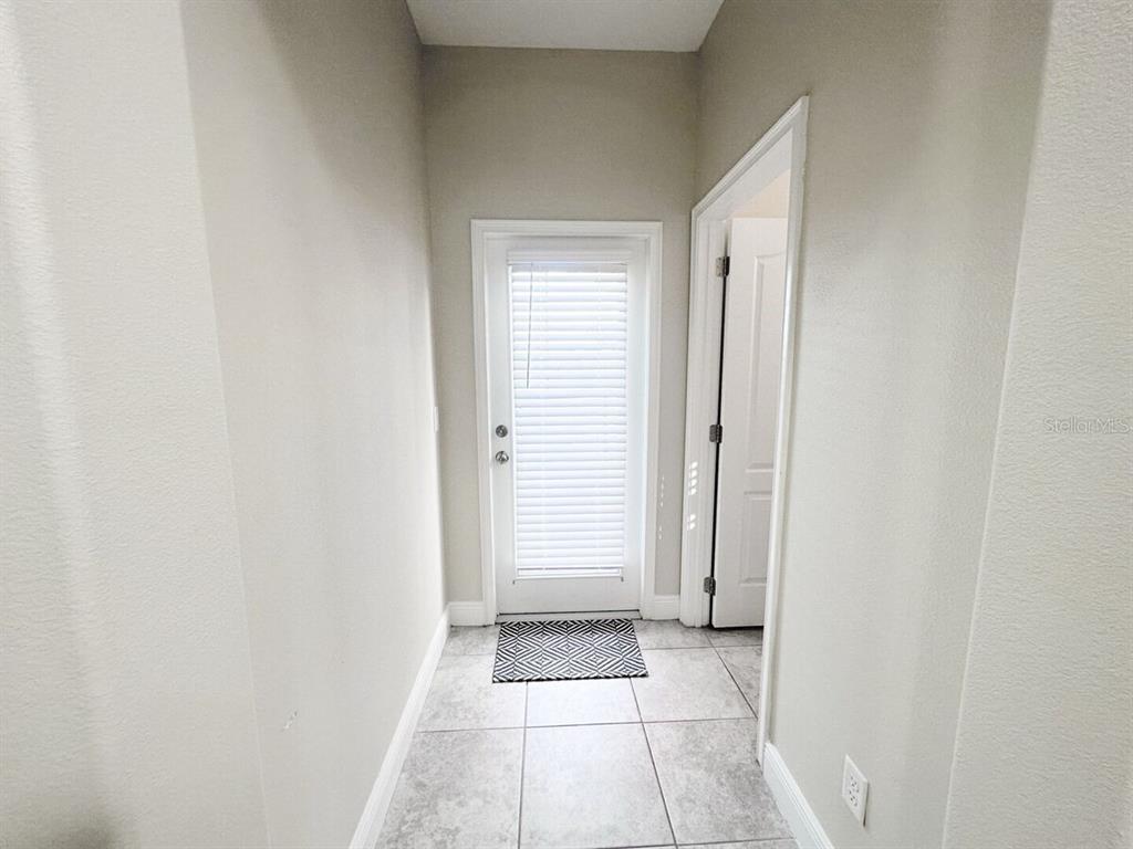 A hallway with light-colored walls, tiled flooring, and a door with white blinds — 162 KENNY BOULEVARD, HAINES CITY, FL