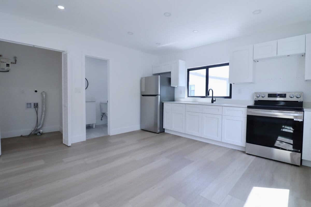 A modern kitchen features white cabinets, stainless steel appliances, and light wood-look flooring — 3040 NW 13th Avenue # 2, Miami FL 33142, MIAMI, FL