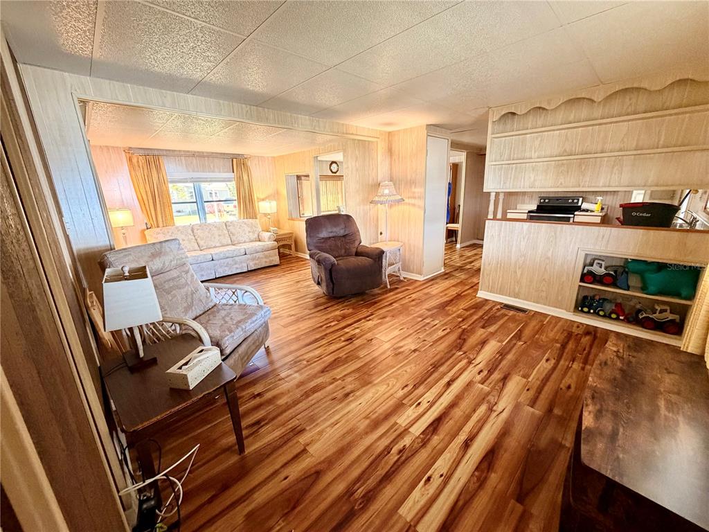 A living room with wood-look flooring, a recliner, a sofa, and built-in wooden shelving — 6363 KILEPA COURT, NORTH PORT, FL